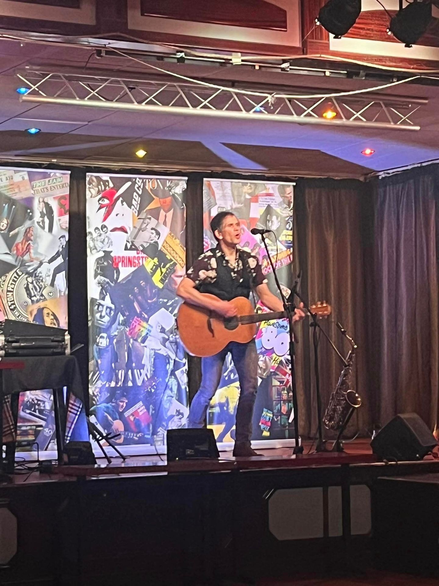 Musician playing acoustic guitar on stage with colorful backdrop and microphone stand.