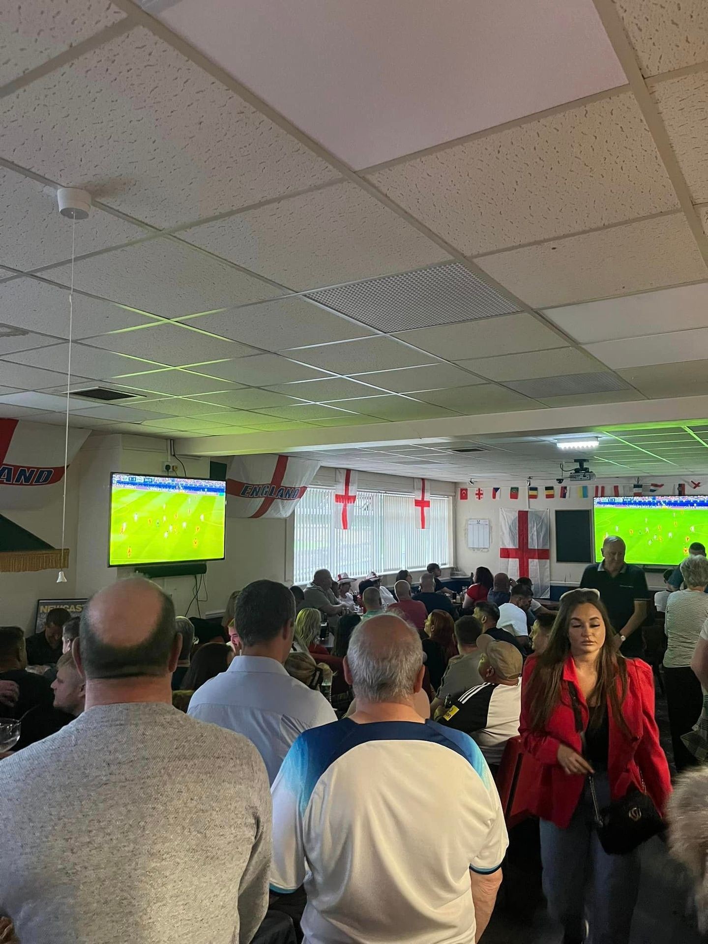 Crowd watching a football match on TV screens in a room decorated with England flags.